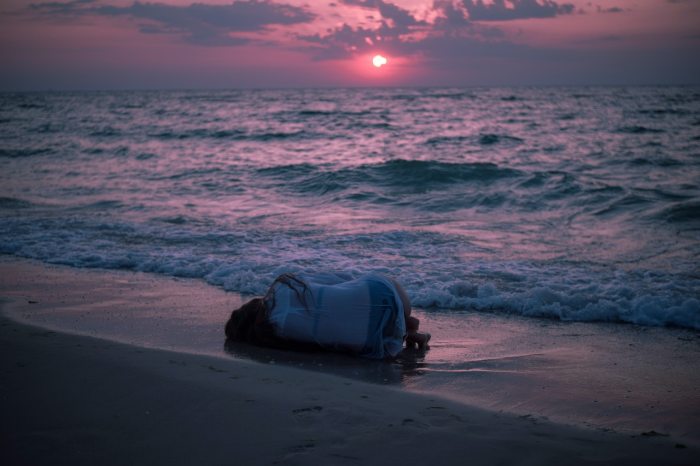 photo of person lying down on beach as the sun set in pinks and blues